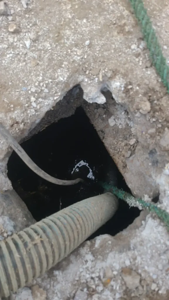 Limpieza de pozos sépticos a vista en primer plano de la apertura de un pozo séptico en el suelo de concreto, con mangueras de succión introducidas en su interior para el proceso de limpieza y vaciado de lodos.