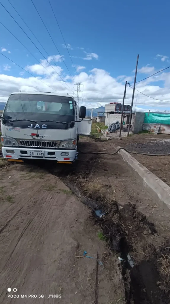 Camión de saneamiento estacionado en un terreno no pavimentado realizando trabajos de limpieza de pozo séptico con manguera de succión.