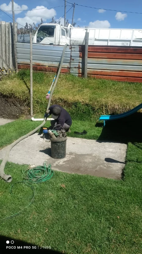Trabajador realizando la succión y limpieza de un pozo séptico en un jardín usando una manguera.